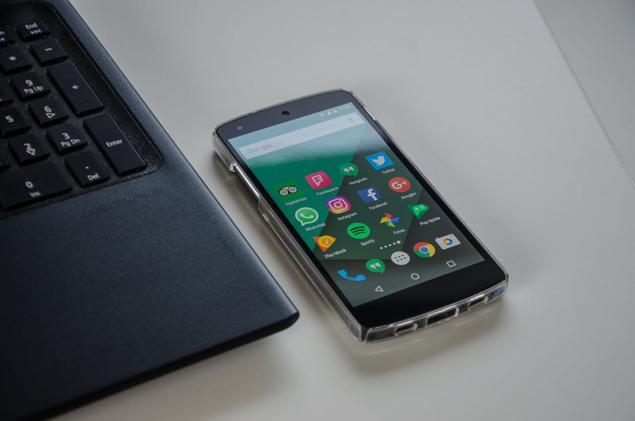 trusted-partner Smartphone on a table showing various social media apps beside a laptop keyboard.