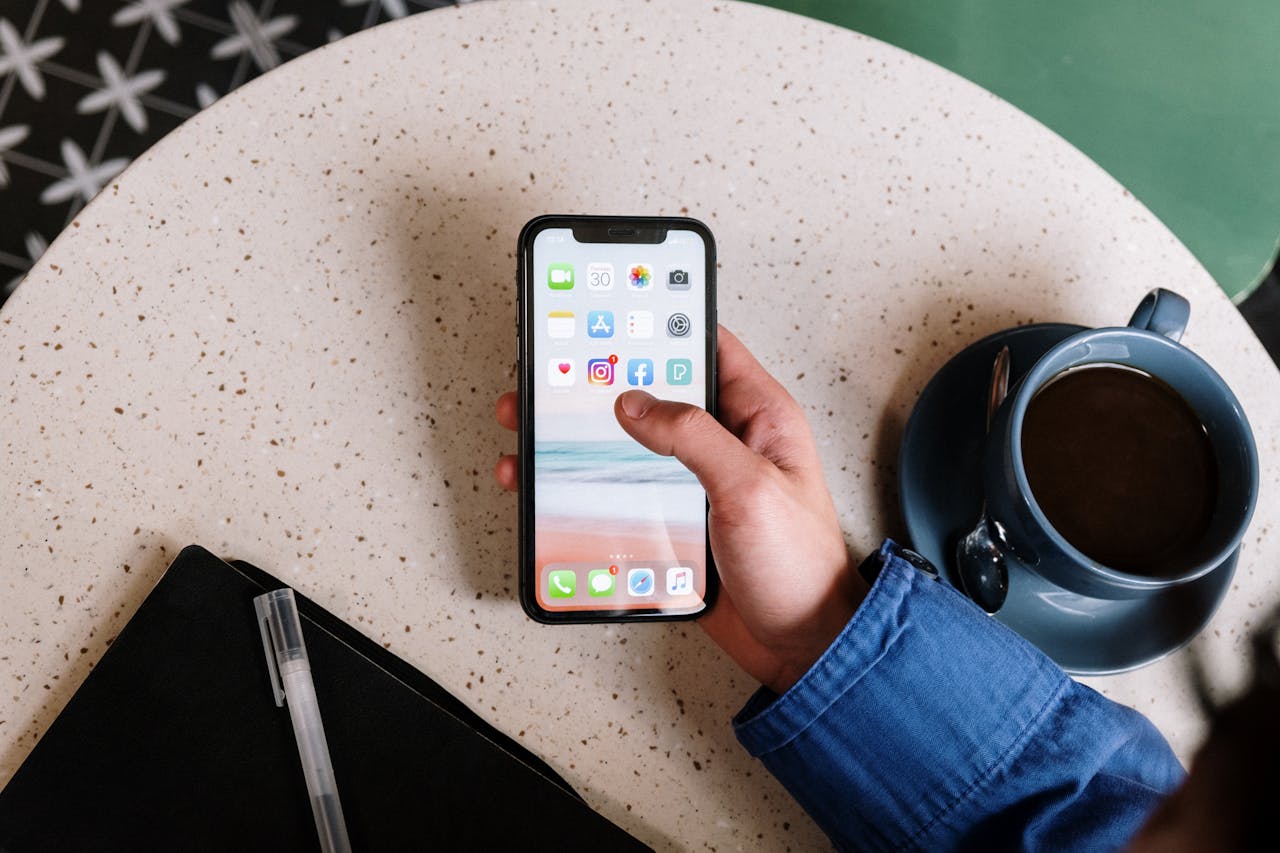 vision Person interacts with smartphone and coffee on a terrazzo table, showcasing apps and casual lifestyle.